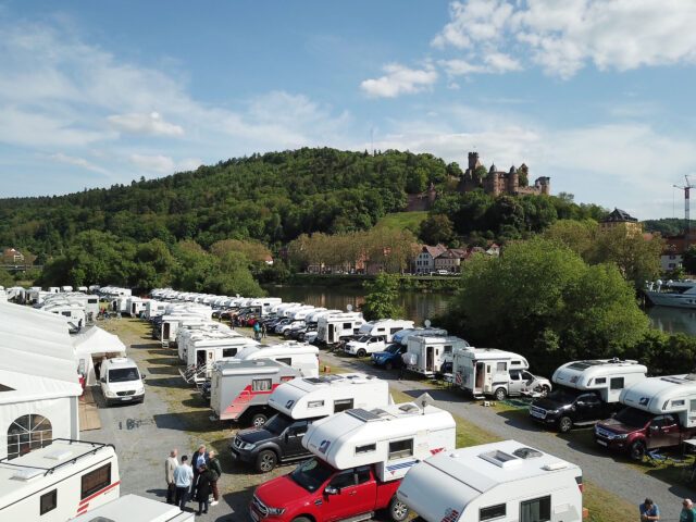Stellplatz mit vielen Tischer-Wohnkabinen aufgereiht am Mainufer, im Hintergrund die Ruine der Burg Wertheim.