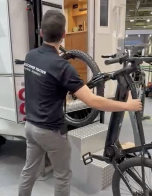 Fahrrad wird am Heckträger einer Tischer Wohnkabine befestigt – Mann von hinten zu sehen.