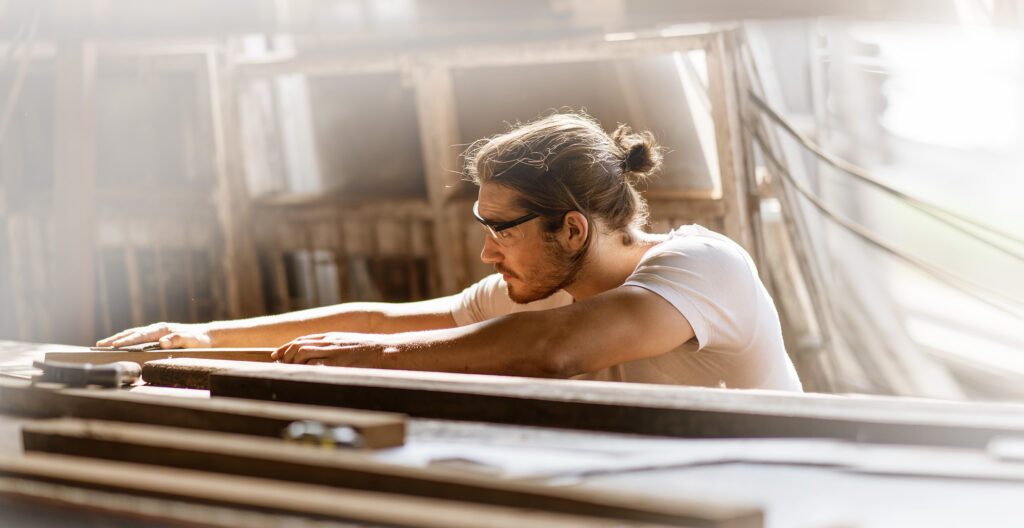 young carpenter man using sandpaper on a piece of wood in workshop .