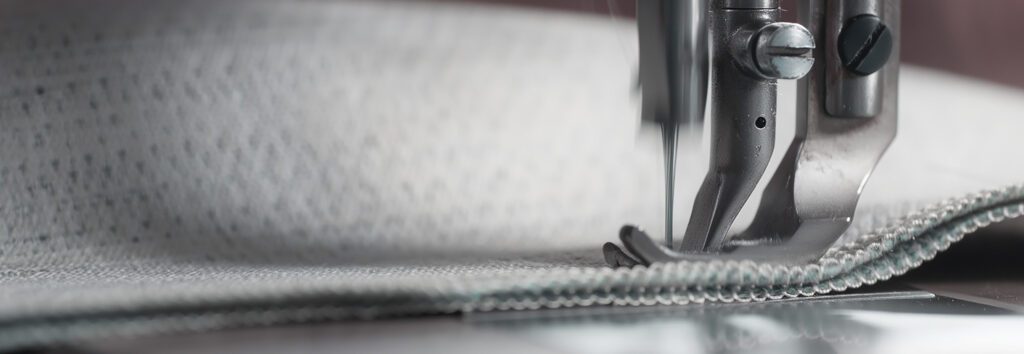 Detailaufnahme einer Nähmaschine beim Verarbeiten eines Stoffes – Symbol für Handarbeit und Präzision.